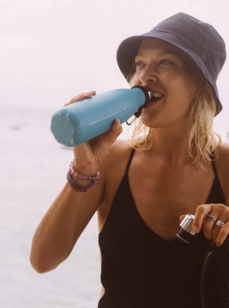 Young woman traveler drinks water from a colored bottle.